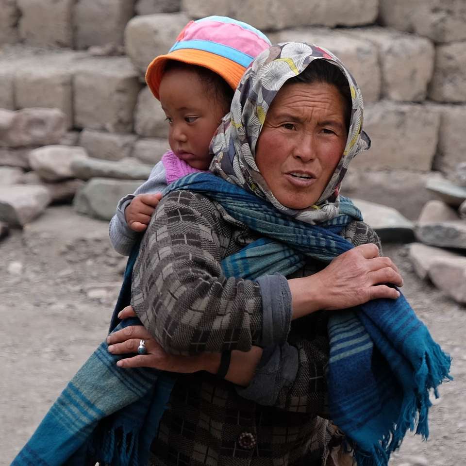 жена, носеща шал, докато носи момиче на гърба си през деня онлайн пъзел