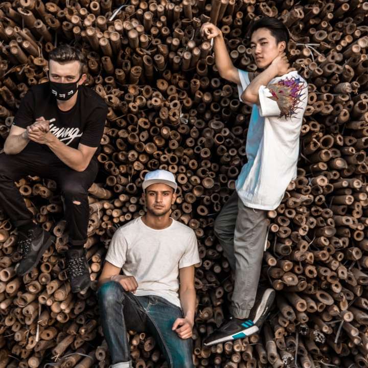 Tres hombres posando junto a la pila de bambúes rompecabezas en línea
