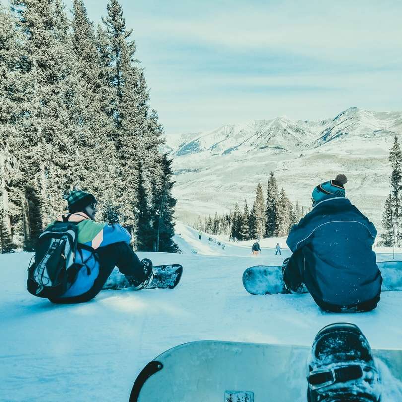 zwei Personen sitzen mit ihren Snowboards auf Schnee Online-Puzzle