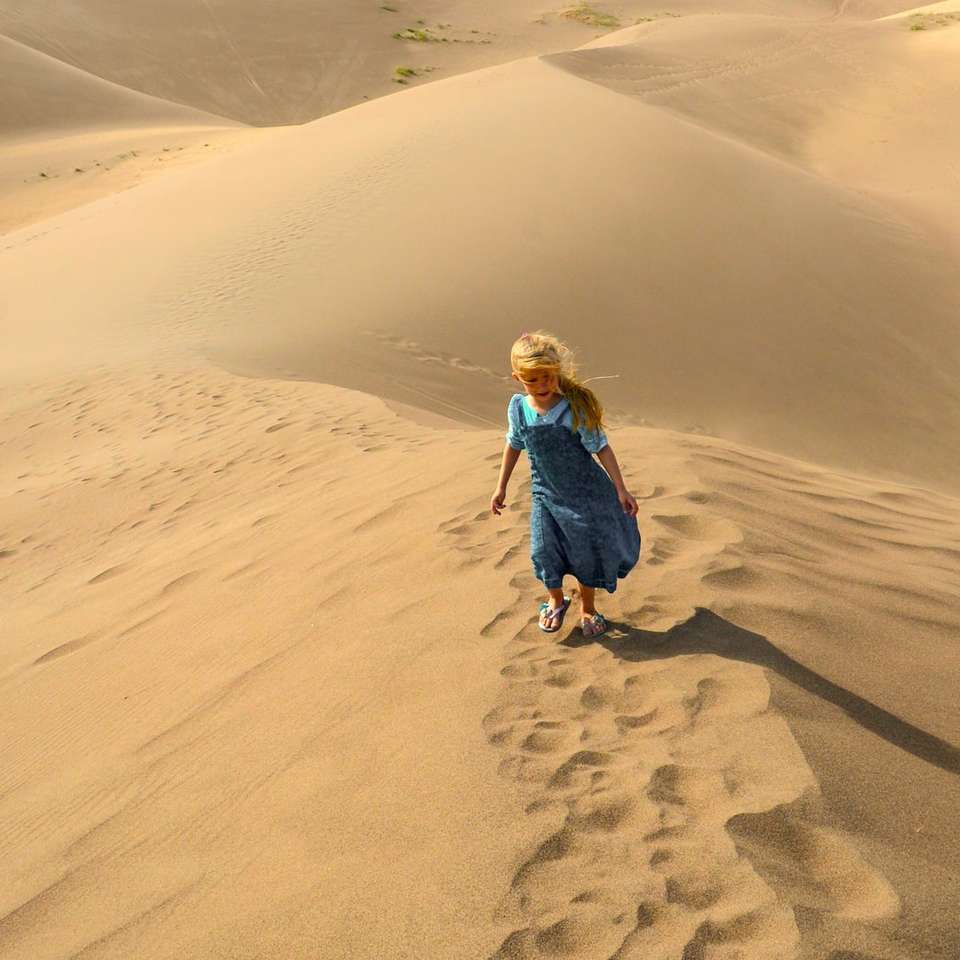 flicka i blå jacka som går på sand på dagtid glidande pussel online