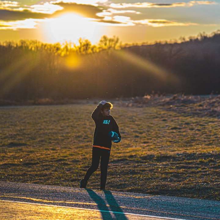 жінка в чорній куртці йде по дорозі під час заходу сонця розсувний пазл онлайн