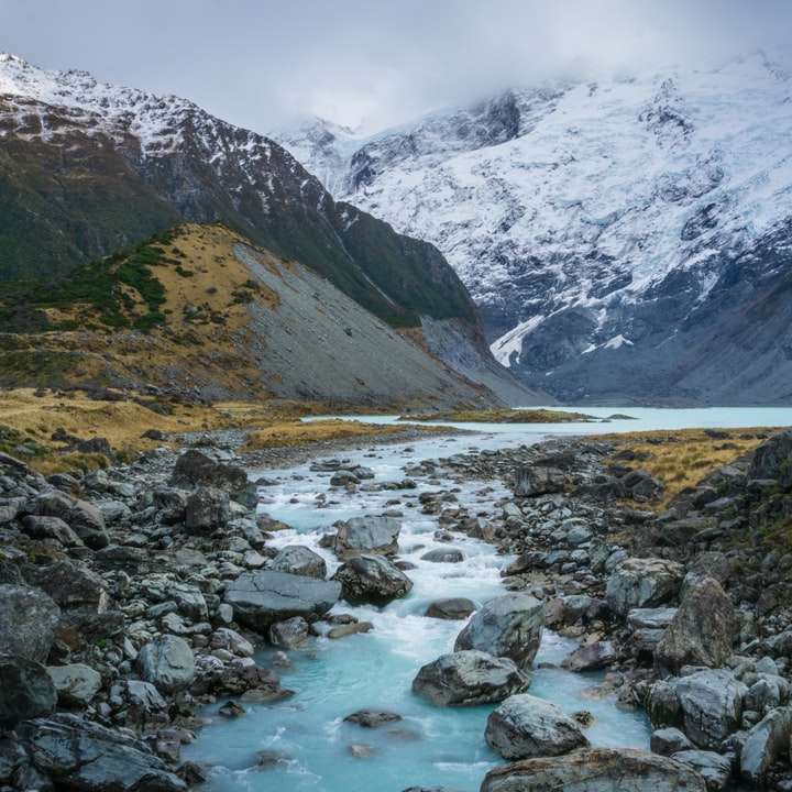 flod med grå stenar nära berget täckt av snö Pussel online