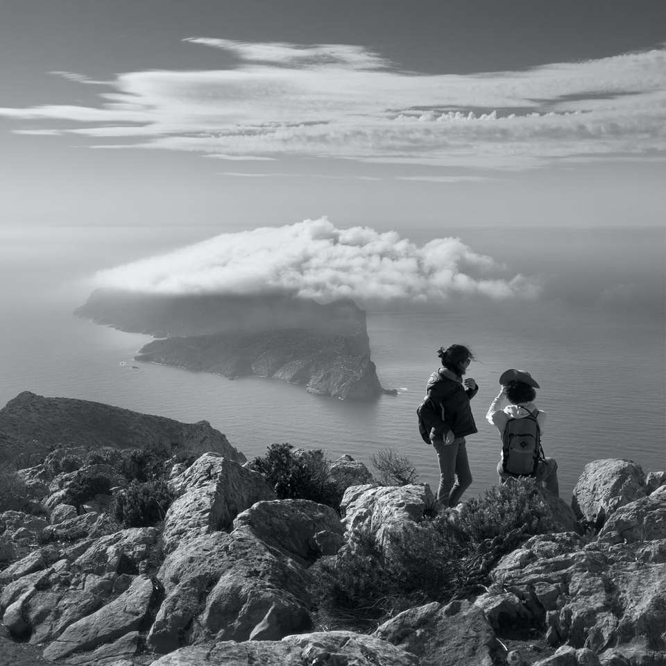grayscale photo of two women on rock beside sea online puzzle