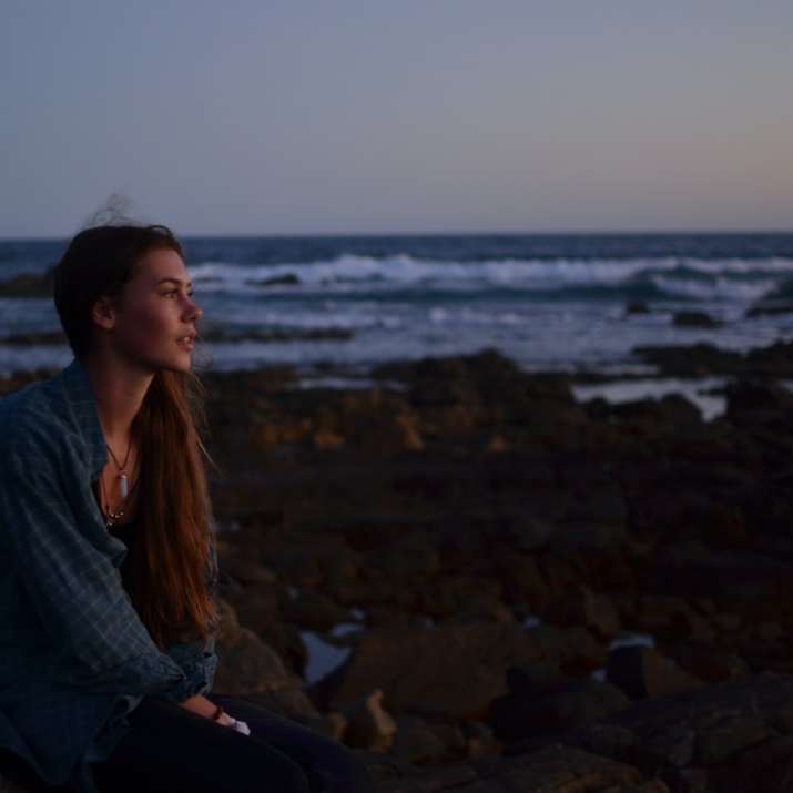 φωτογραφία γυναίκας που κάθεται πάνω σε βράχους κοντά στην παραλία online παζλ
