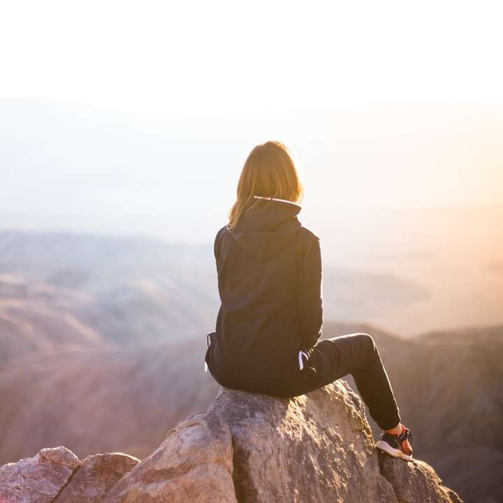 osoba siedząca na szczycie szarej skały z widokiem na góry puzzle online