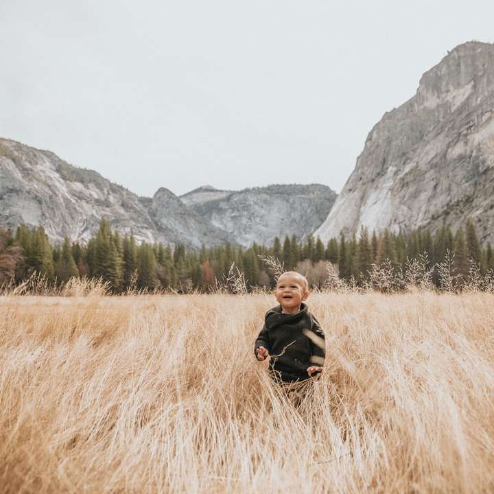 chlapec v černé bundě stojí na hnědé trávě poblíž hory online puzzle