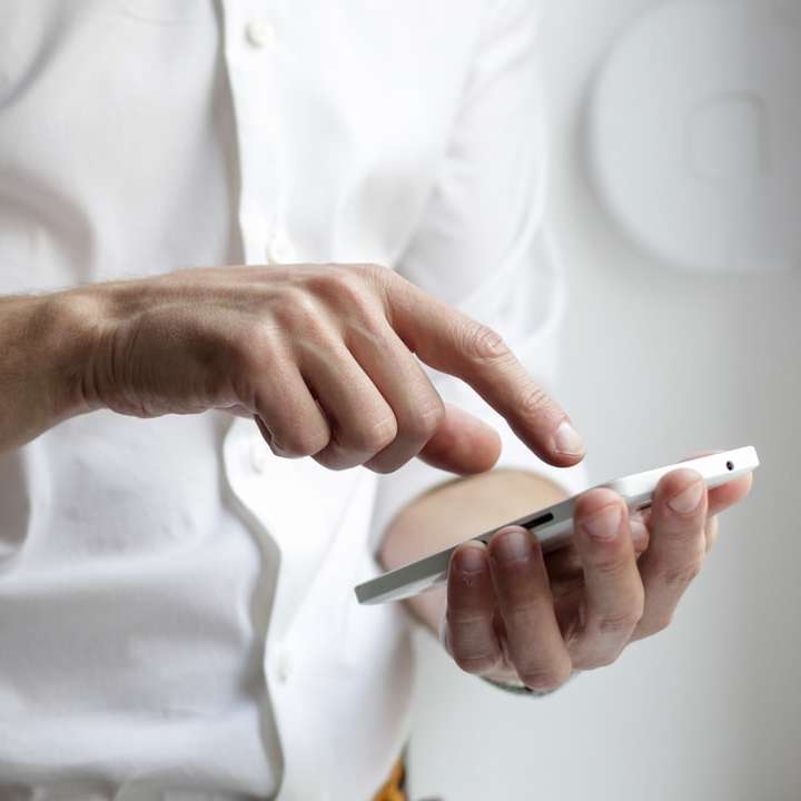 Personne tenant un smartphone Android blanc en chemise blanche puzzle en ligne