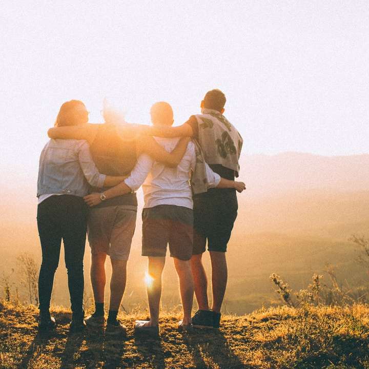 mani di quattro persone avvolgono le spalle mentre guardano il tramonto puzzle scorrevole online