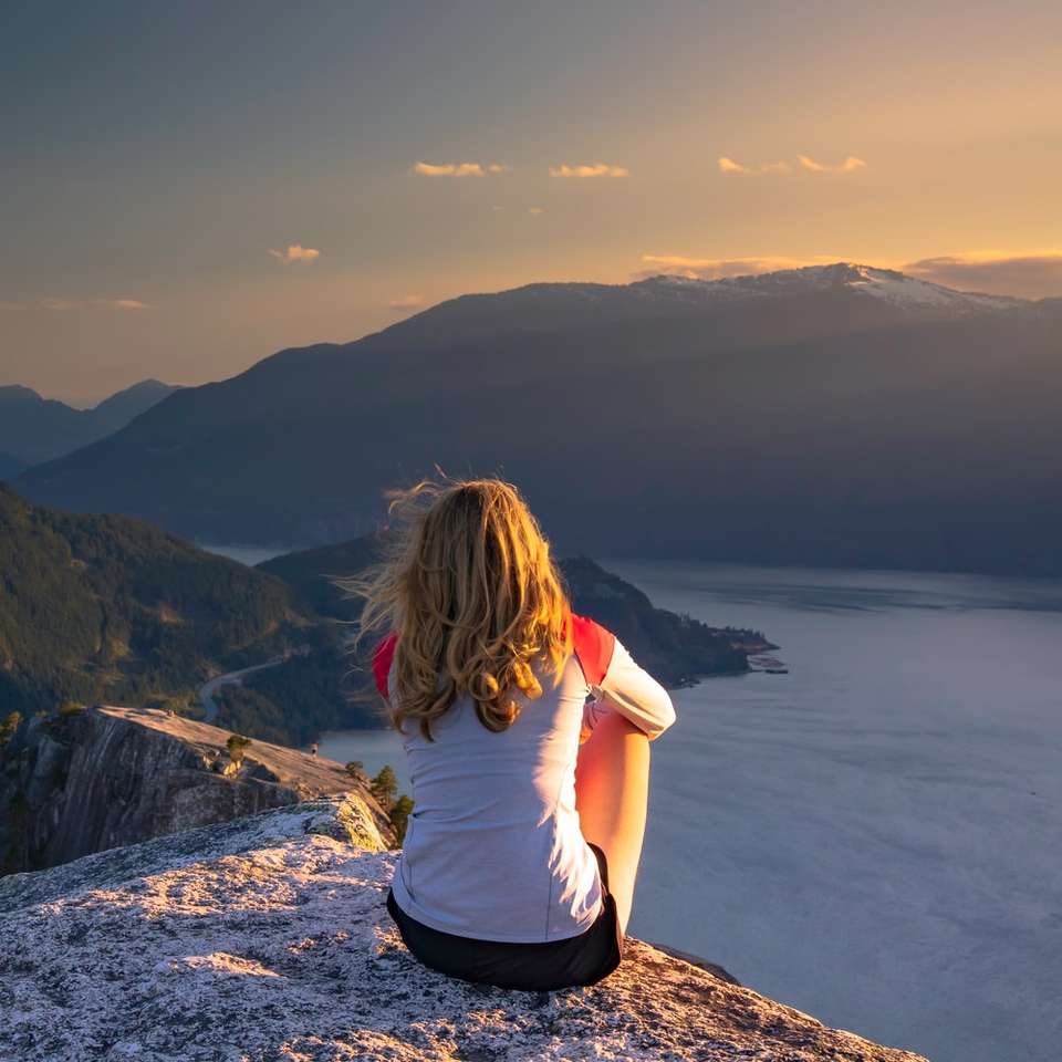 Femme assise au sommet de la montagne au coucher du soleil. puzzle coulissant en ligne