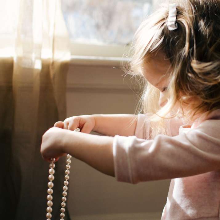 Девушка держит в комнате белое жемчужное ожерелье онлайн-пазл