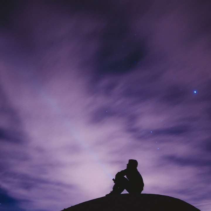 osoba siedząca na czarnej powierzchni patrząc w niebo puzzle przesuwne online