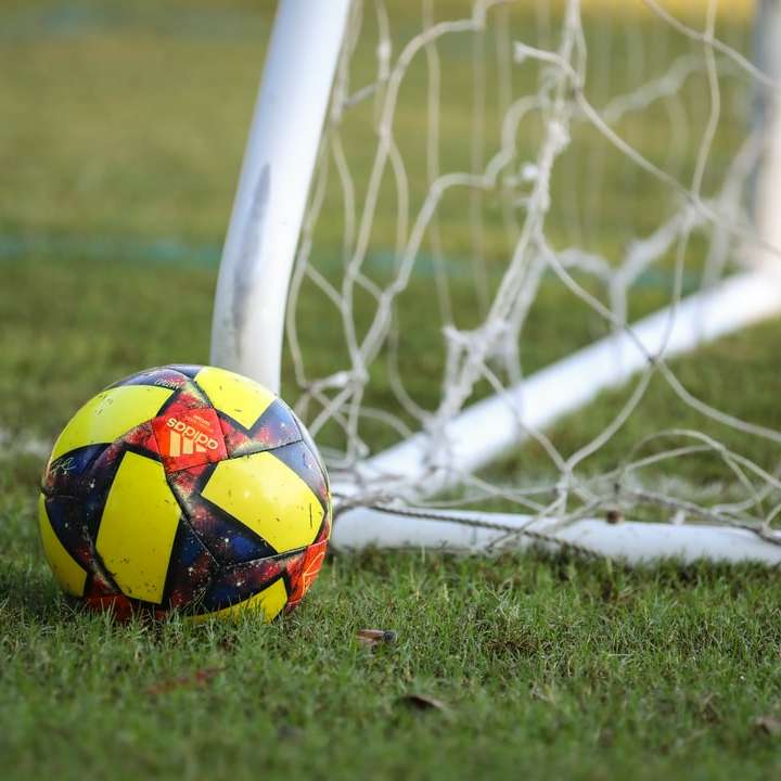 Balón de fútbol rojo, azul y amarillo en el campo de hierba verde puzzle deslizante online