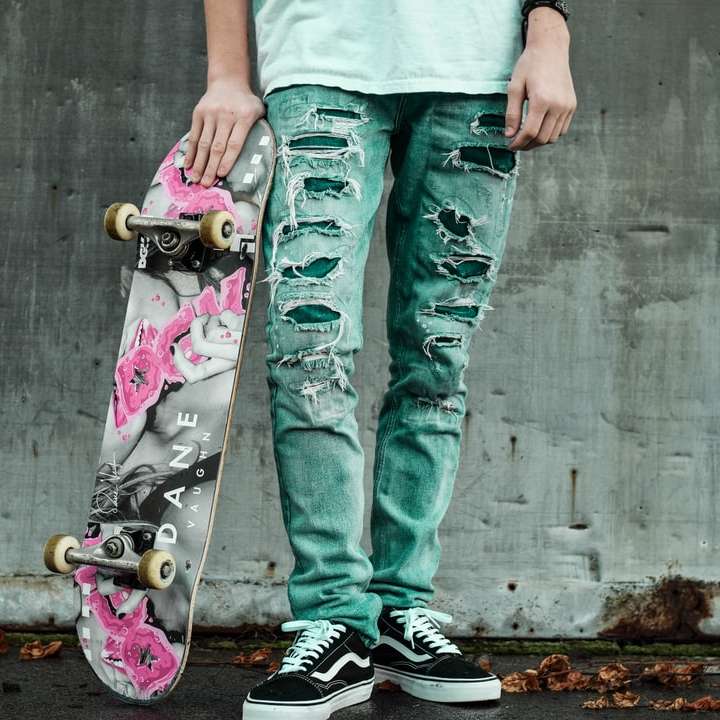 Mann, der neben Wand steht, die graues und rosa Skateboard hält Online-Puzzle