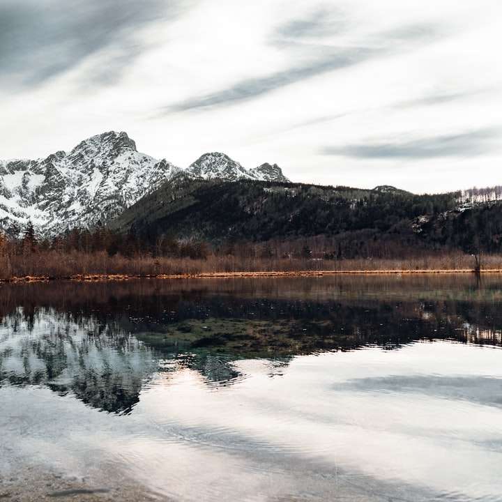 lake near snow covered mountain under cloudy sky sliding puzzle online