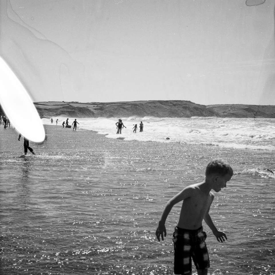 grayscale photo of boy holding surfboard on beach online puzzle
