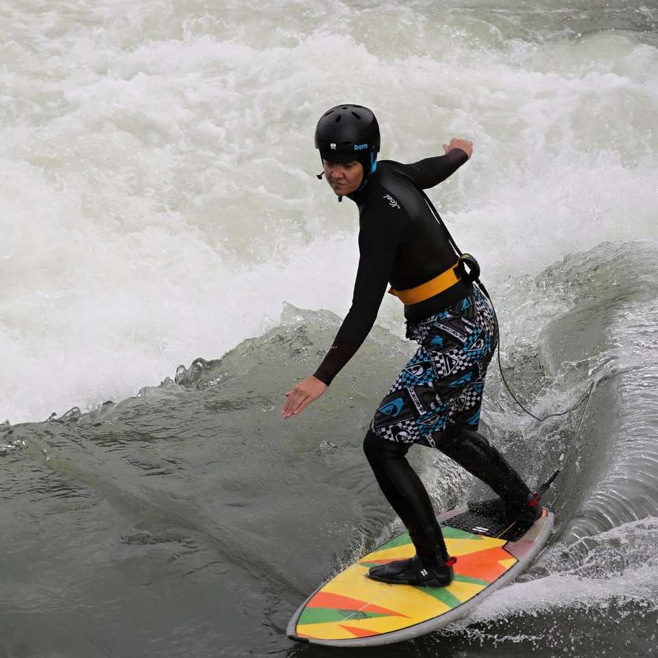 мъж в синьо-черен хидрокостюм, яздещ жълта дъска за сърф плъзгащ се пъзел онлайн