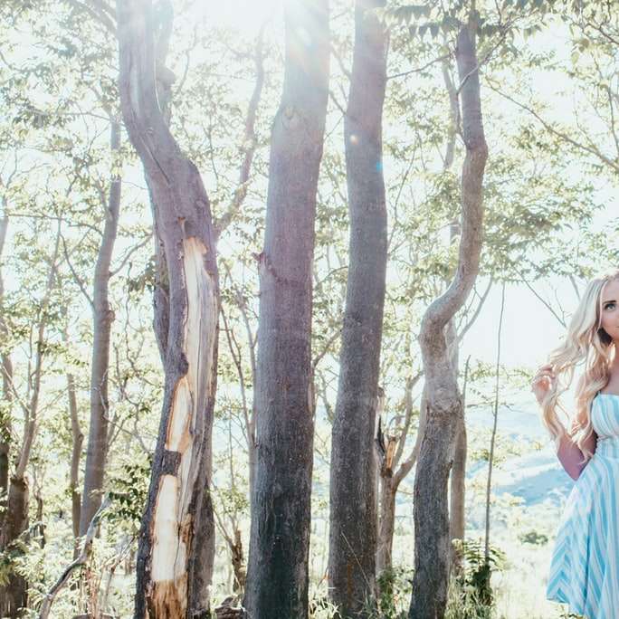 kvinna i vit och blå randig klänning som står under träd Pussel online