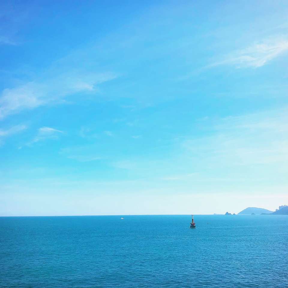 Persona con camisa negra de pie sobre el mar azul bajo un cielo azul rompecabezas en línea