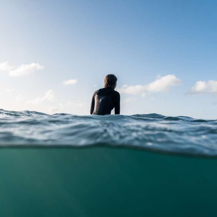donna in camicia nera che si siede sull'acqua di mare durante il giorno puzzle scorrevole online