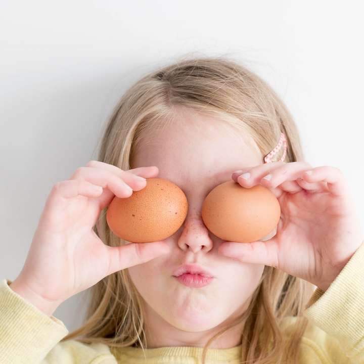 момиче, което държи две яйца, докато го слага на очите си онлайн пъзел
