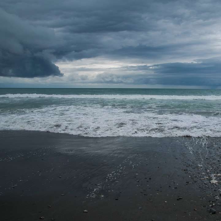 морские волны разбиваются о берег под бело-голубым облачным небом онлайн-пазл