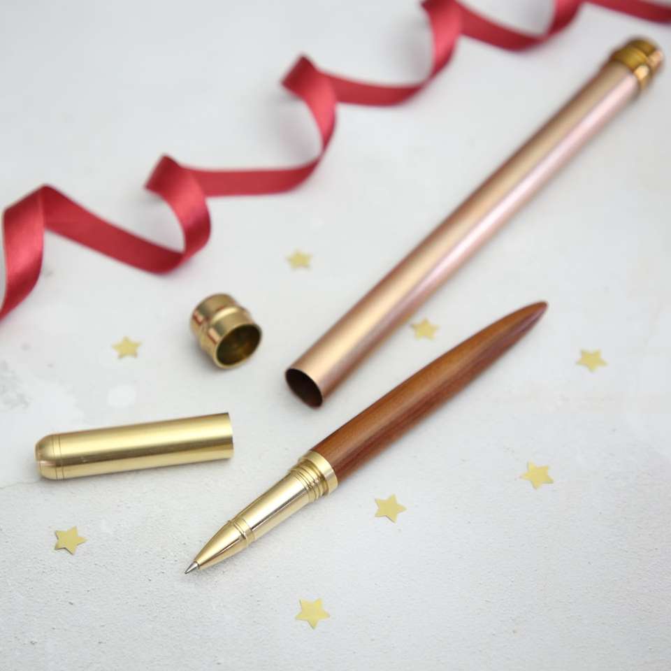 brass-colored pen with case beside red ribbon online puzzle
