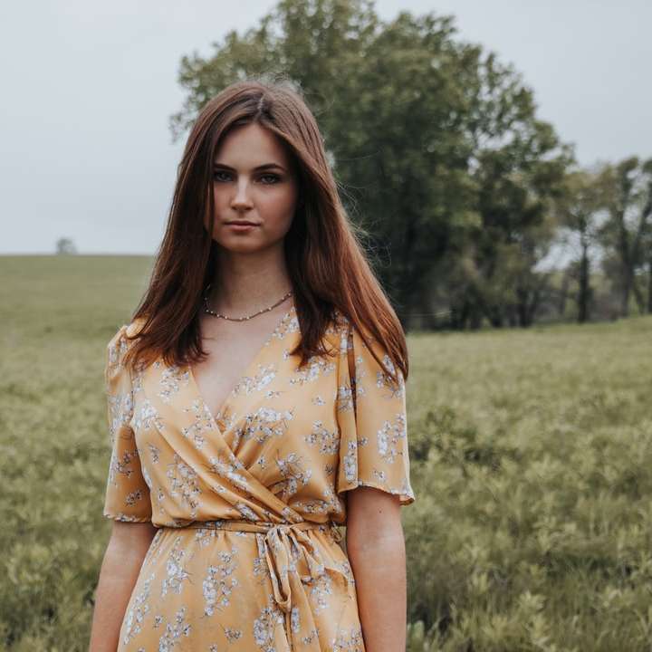 Femme en robe à fleurs jaune debout sur le champ d'herbe verte puzzle en ligne