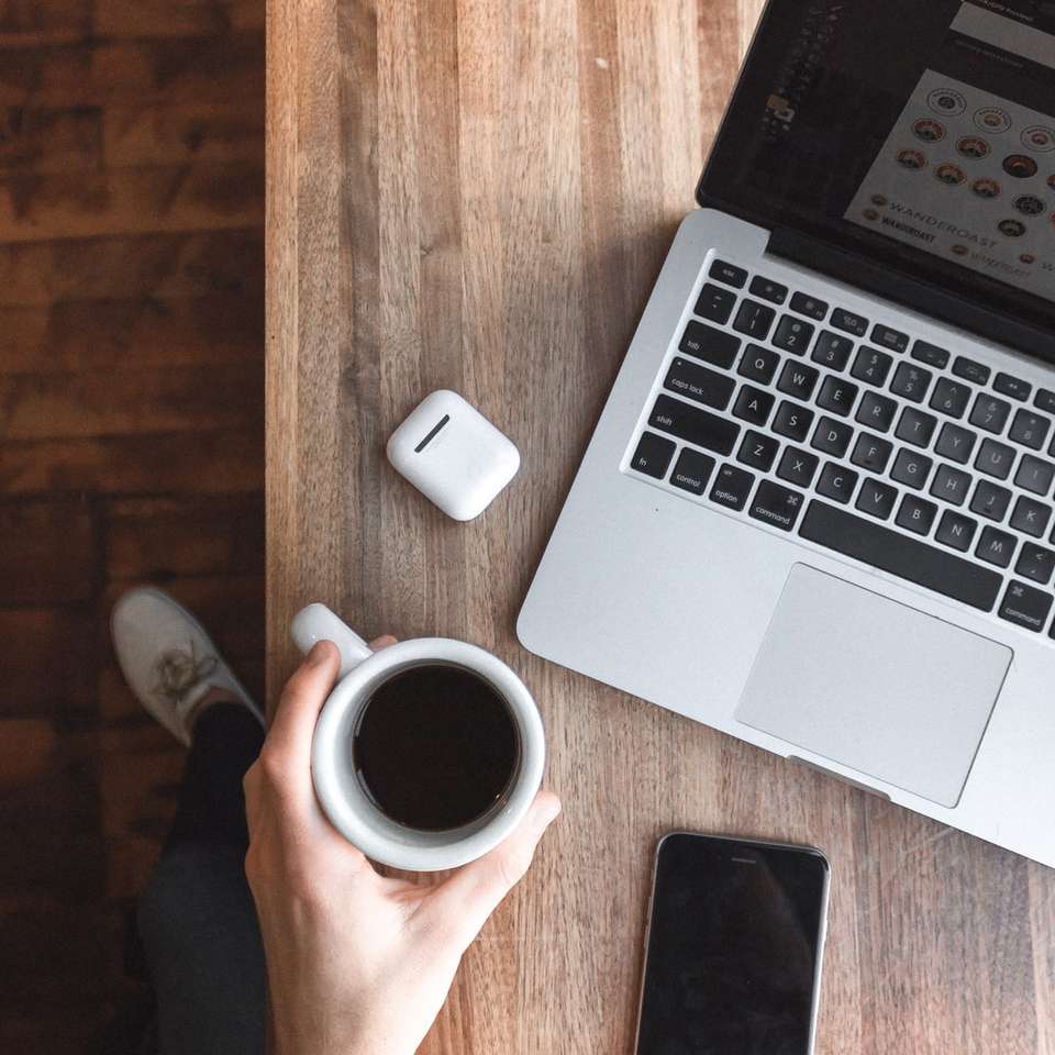 Persona sosteniendo una taza de café junto a la computadora portátil gris puzzle deslizante online