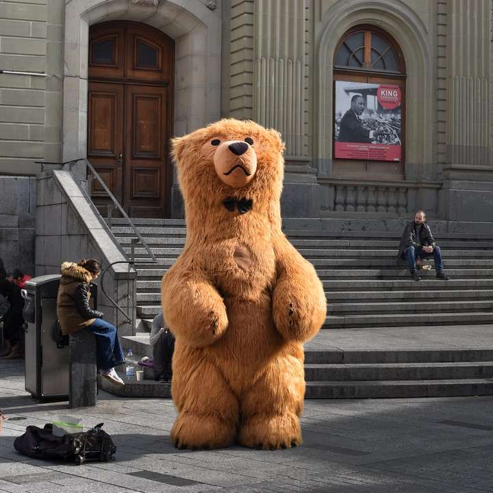 Талисман бурого медведя стоит перед зданием онлайн-пазл