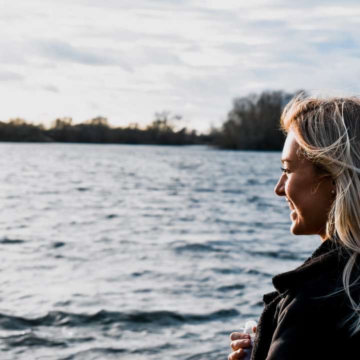 woman in black jacket standing near body of water sliding puzzle online