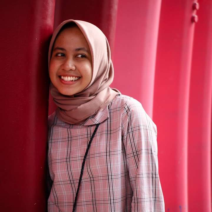 χαμογελαστή γυναίκα που ακουμπά στον κόκκινο τοίχο συρόμενο παζλ online