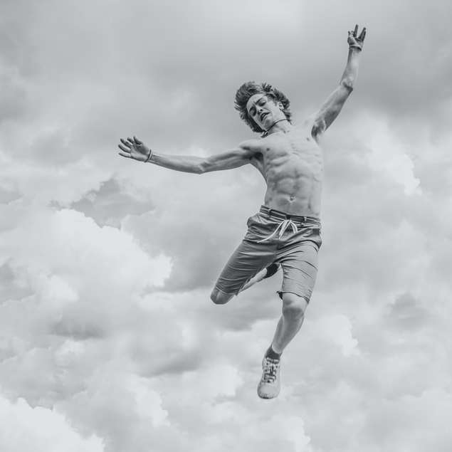 grayscale photo of person jumping overlooking clouds sliding puzzle online