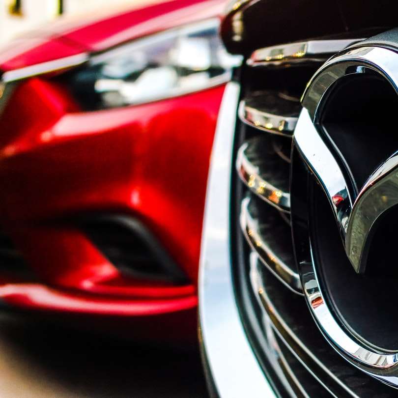 Emblema Mazda sulla griglia accanto all'auto rossa parcheggiata puzzle online