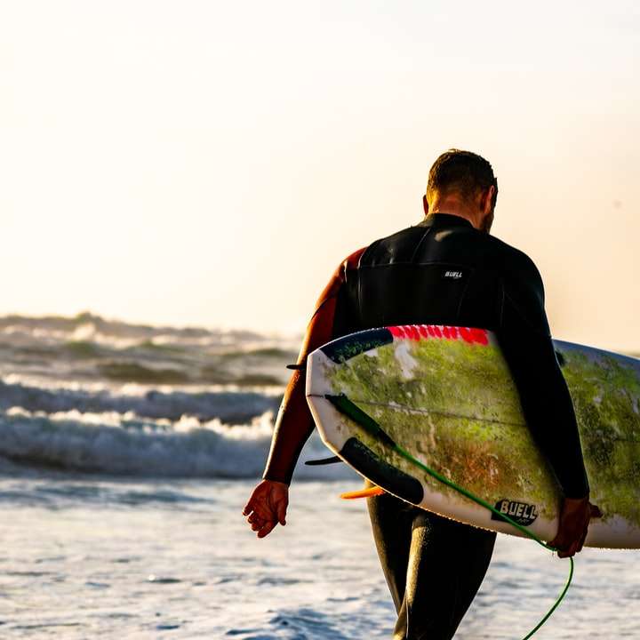 muž nesoucí bílý Surf při chůzi směrem k moři online puzzle