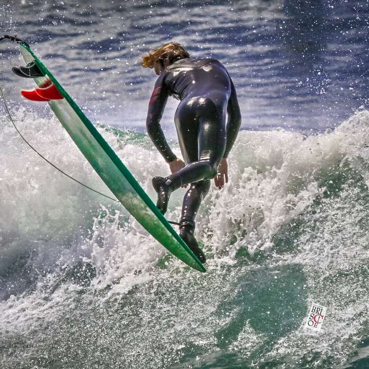 мъж в черен мокър костюм, каране на зелен сърф през деня плъзгащ се пъзел онлайн