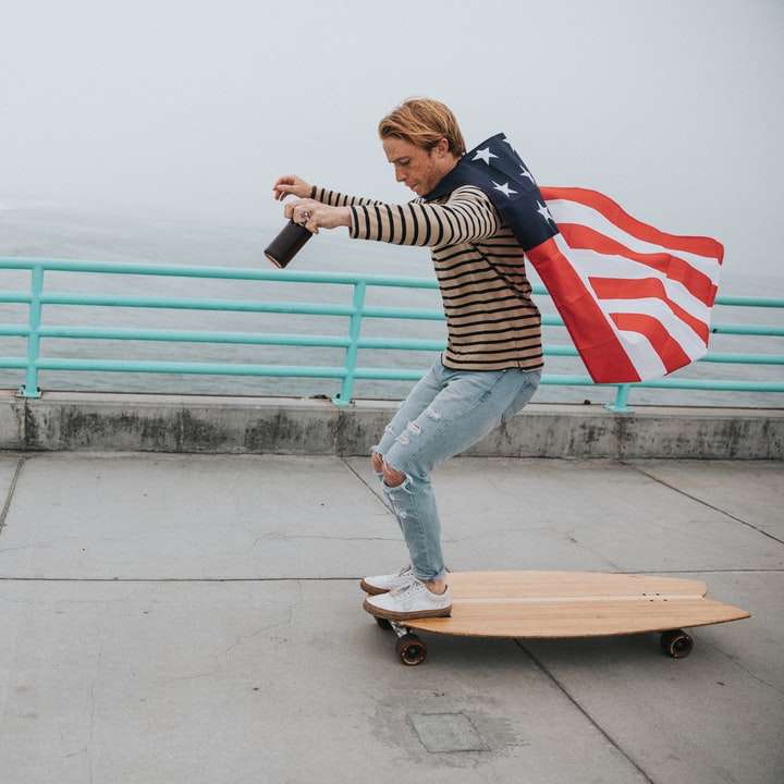 Mann, der Umhang der US-Flagge trägt, während er auf Longboard reitet Schiebepuzzle online