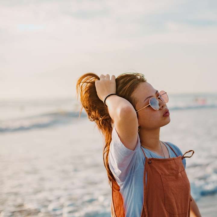 donna in camicia blu che indossa occhiali da sole in piedi sulla spiaggia puzzle scorrevole online