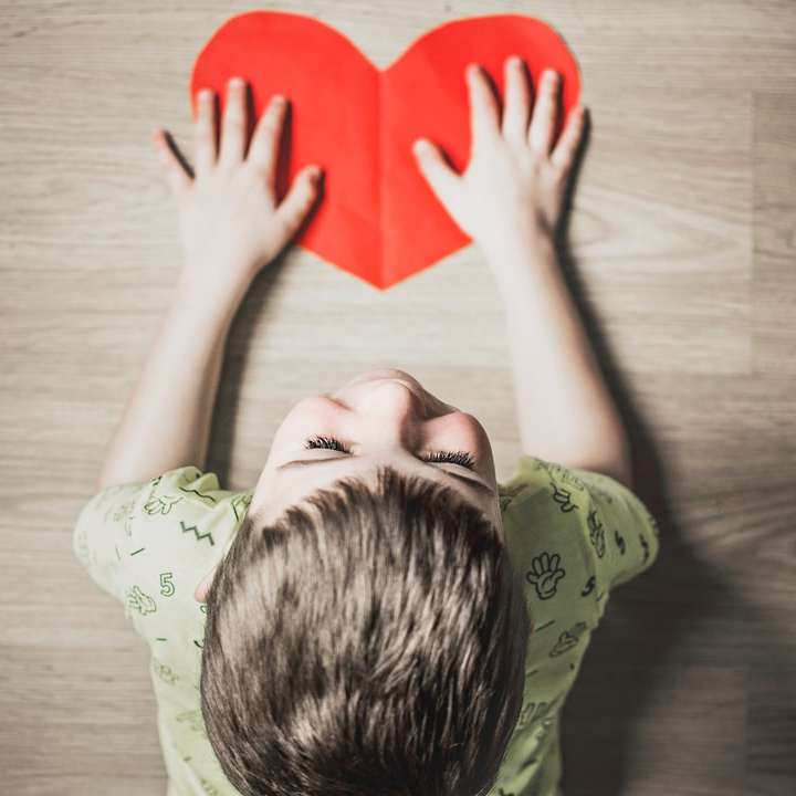 pojke i grön skjorta som håller rött pappershjärtsskär Pussel online