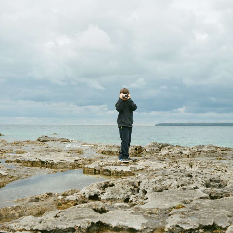 człowiek stojący na formacji skalnej w pobliżu zbiornika wodnego puzzle online