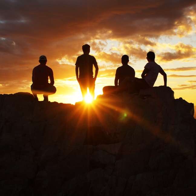 fotografia de silhueta de quatro pessoas em um penhasco durante o pôr do sol puzzle deslizante online