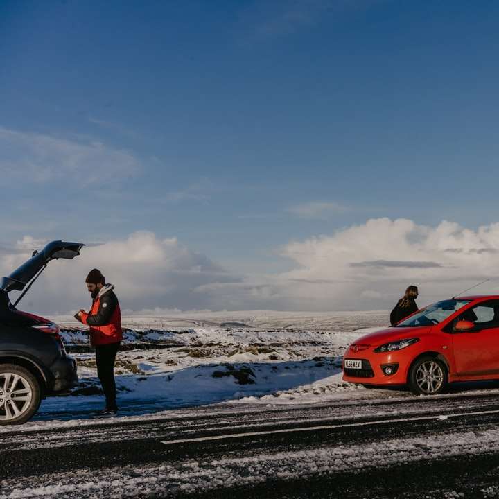 bărbat în jachetă maro care stă lângă mașină roșie alunecare puzzle online