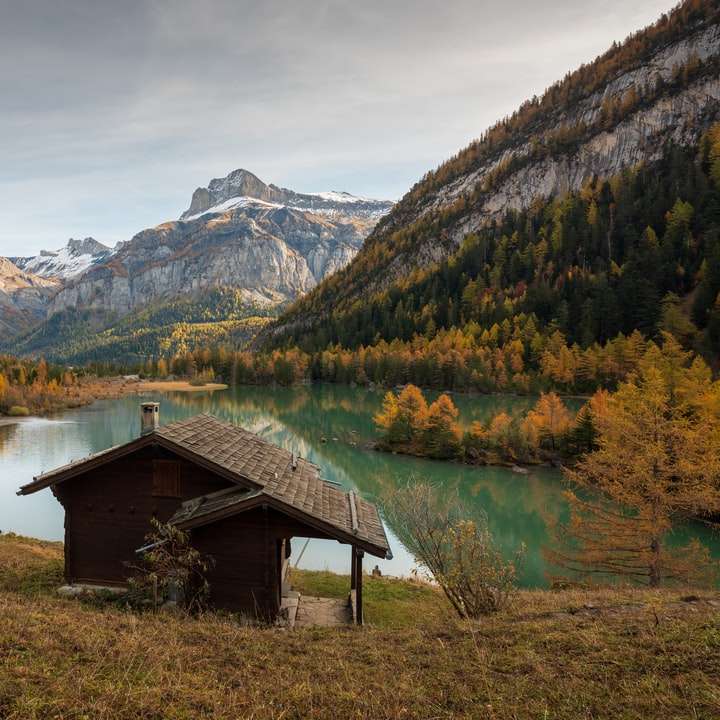 casa de madeira marrom no lago perto de montanhas verdes e marrons puzzle deslizante online