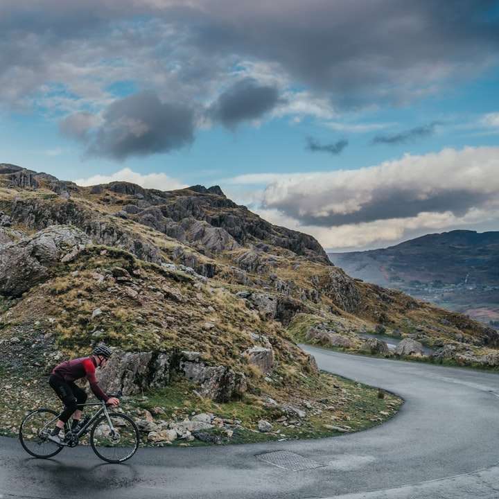 uomo in giacca rossa in bicicletta sulla strada vicino alla montagna puzzle online