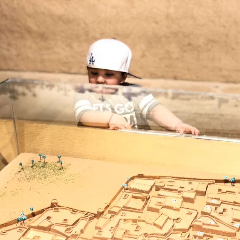 Kind im weißen Helm, der tagsüber auf braunem Sand liegt Online-Puzzle