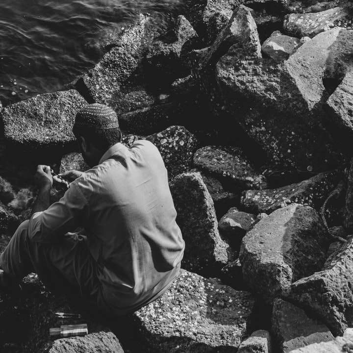Mann in schwarzer Jacke und Hose sitzt auf Felsen nahe Körper Schiebepuzzle online