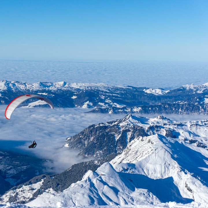 Persona montada en paracaídas sobre montañas cubiertas de nieve rompecabezas en línea