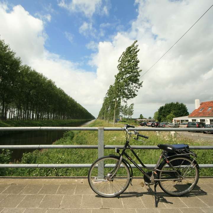 緑の金属柵の横に駐車された黒い自転車 スライディングパズル・オンライン