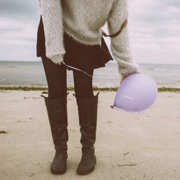 женщина в серой шубе и черных штанах стоит на пляже онлайн-пазл