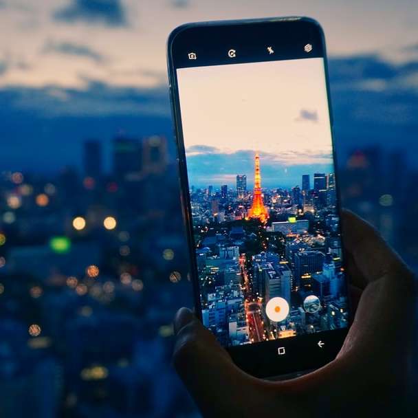 person holding smartphone taking photo of city buildings sliding puzzle online