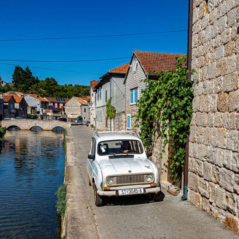 biały samochód zaparkowany obok brązowego muru w pobliżu zbiornika wodnego puzzle online